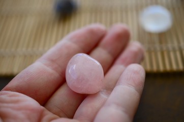 Holding Rose Quartz, natural lighting. Pink, romantic healing crystal. Pastel rose quartz chunks. Person holding small pink gemstone. Light pink, rough and tumbled crystals. 