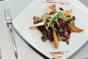 Salad with fried mushrooms, fried potatoes, greens on a plate on the table