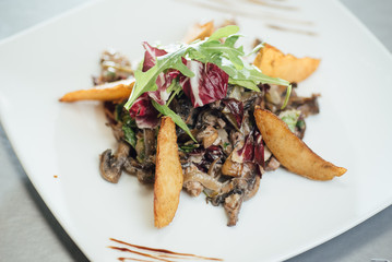 Salad with fried mushrooms, fried potatoes, greens on a plate on the table