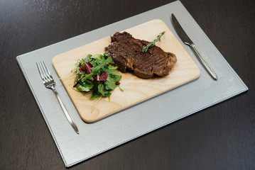 A piece of fried meat and greens on a wooden cutting board on the table