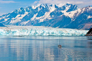 A tiny sailboat approaches the towering Hubbard Glacier in Alaska