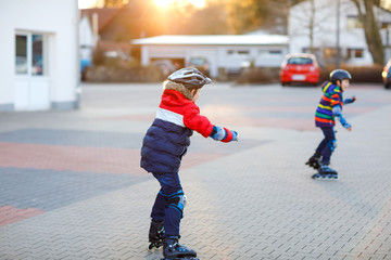 Two little kids boys skating with rollers in the city. Happy children, siblings and best friends in...