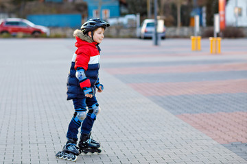 Cute school kid boy skating with rollers in the city. Happy healthy child in protection safety clothes skating with rollers. Active schoolboy making sports and learning to skate on inline skater.