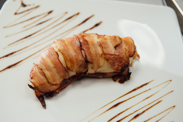 Meat with fried bacon on a white plate on the table