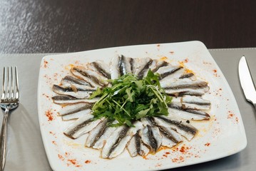 Freshly Spiced Sprat with Greens on a Plate on the Table