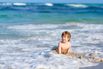 Fototapeta na wymiar Adorable little blond kid boy having fun on ocean beach. Excited child playing with waves, swimming, splashing and happy about family vacations in Miami, Florida, USA.