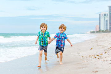 Two happy little kids boys running on the beach of ocean. Funny cute children, sibling and best friends making vacations and enjoying summer on stormy windy day. Healthy kids on beach of Miami, USA