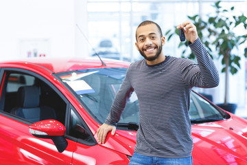 Handsome African man showing keys to his new car at the dealership
