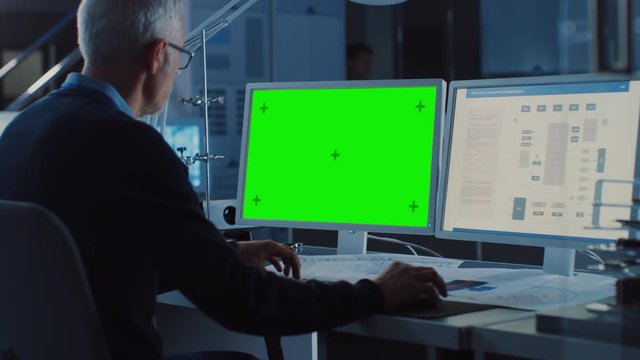 Professional Engineer Works on Computer with Green Mock-up Screen and Electronics Motherboard Blueprint Showing Display. In the Background Industrial Electronics Design Agency. Over the Shoulder Shot