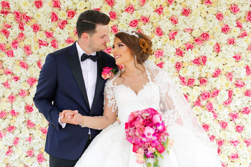 beautiful bride and groom on the background of a wall of flowers.