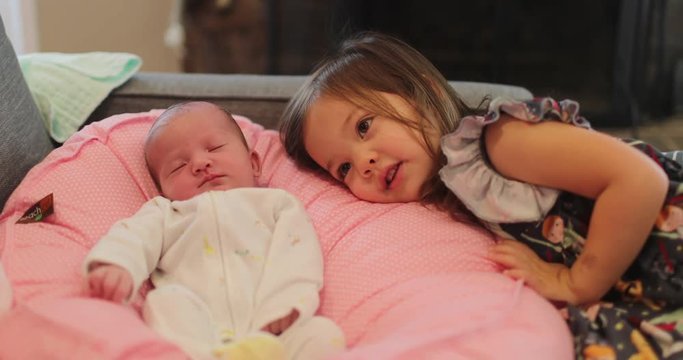 Sweet moments between newborn and big sister as sister kisses baby on the head while lounging.