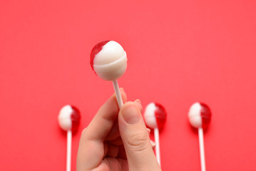 Lollipop in female hand on red background. Space for text or design.