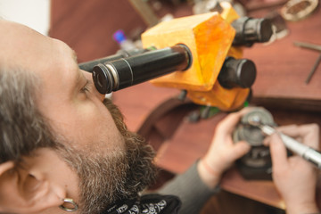 Fototapeta premium Professional craftsman using microscope while repairing jewelry on his vintage workbench
