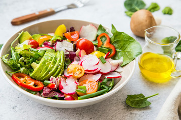 Healthy salad bowl with fresh vegetables, avocado, tomatoes, pepper, radishes, green arugula, onion, spinach and lettuce in a bowl with olive oil and hemp seeds