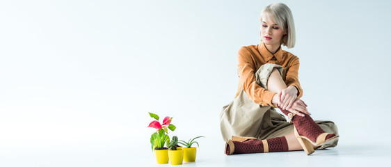 Obraz na płótnie Canvas panoramic shot of beautiful stylish girl sitting with flower pots on white with copy space