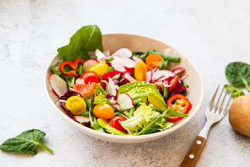 Healthy salad bowl with fresh vegetables, avocado, tomatoes, pepper, radishes, green arugula, onion, spinach and lettuce in a bowl with olive oil and hemp seeds