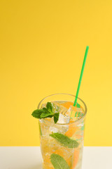 Cocktail with lemon and mint on a yellow background. Copy space.