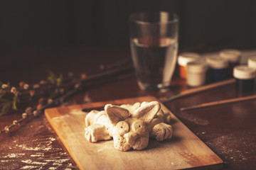 Artist paints religious objects. Easter bunny prepared coloring lying board. Branches willow lilac with blooming green leaves. Paint jars tubes with brushes glass water.