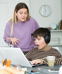 Boy in headphones playing at laptop and  having quarrel with mother