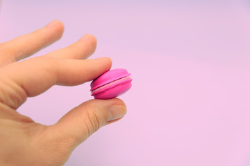 Female fingers hold a pink macaroon on a pink background. Rubber fake, bad imitation