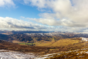 A view of snowy mountain slopes with several other snowy summit in the background under a majestic blue sky and white clouds