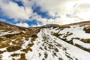 Fototapeta na wymiar A snowy mountain path under a majestic blue sky and white clouds