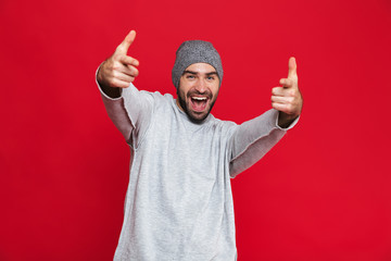 Image of unshaved man laughing and pointing fingers on camera isolated over red background