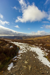 A snowy mountain path under a majestic blue sky and white clouds