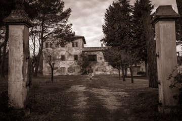 black & white young man with a suitcase walking in front of a creepy  old abandoned house