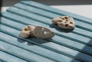 Three small sea stones, found on the seashore, with holes made by the sea, lie on a wooden blue table, hammered together from boards.