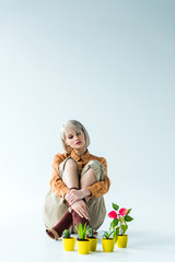 beautiful stylish blonde girl sitting near flower pots on white with copy space