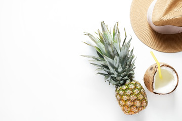 Summer mood concept. Tropical background with ripe organic pinapple with leafy crown, cracked coconut with milk and straw, broad brim hat. Flat lay, top view, copy space, isolated.