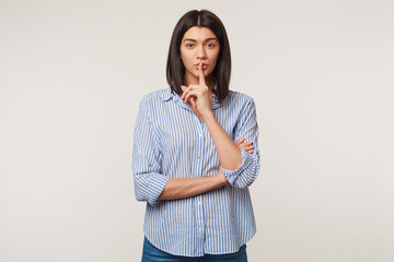 Indoor portrait of a beautiful dark haired girl with swarthy complexion making silence gesture...