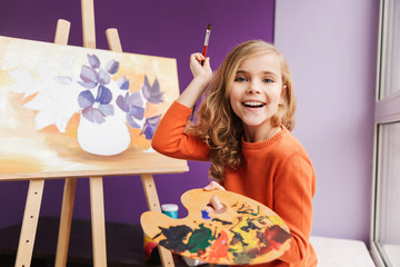 Cute little girl drawing a picture on canvas