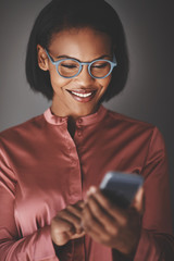 Fototapeta premium Smiling African businesswoman using her cellphone against a gray