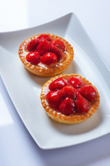 Basket-cakes with mascarpone cheese and decorated with strawberry on white plate. High Key. Close up. Selective focus. Top view.