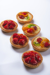 Basket-cakes with mascarpone cheese and decorated with different fruit on white plate. High Key. Close up. Selective focus. Top view.