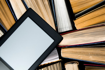 Fototapeta premium The e-book with a white screen lies on the open multi-colored books that lie on a dark background, close-up