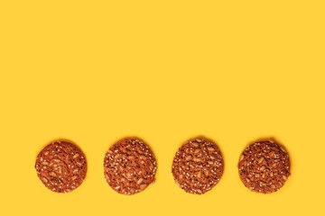 Tasty oatmeal cookies with nuts and seeds on a yellow background.