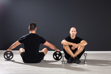 Fototapeta premium two fit males sitting at the floor of the gym studio,looking in opposite direction,having Pilates equipment around them