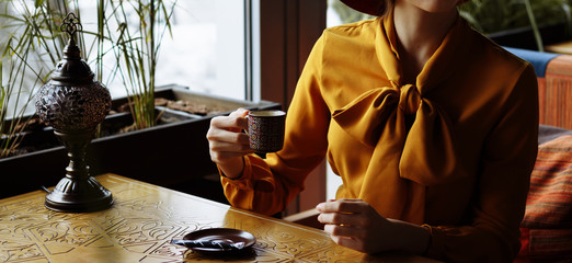 girl in a cafe with a cup of coffee and a hat.portrait of sensual young girl wearing floppy hat and blouse with bow. Beautiful brunette woman in cafe holding cup of coffee