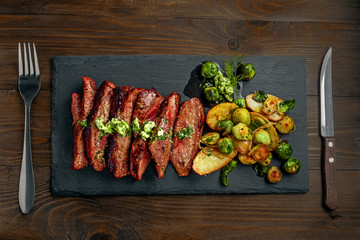 Hanger medium-rare stake with vegetables garnish on a black stone board. Delicious dinner. Top view...