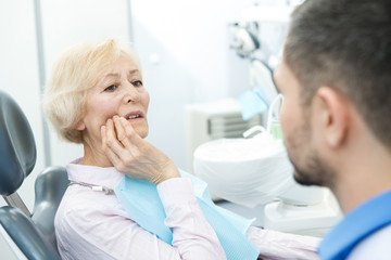 Senior woman suffering from toothache visiting dentist