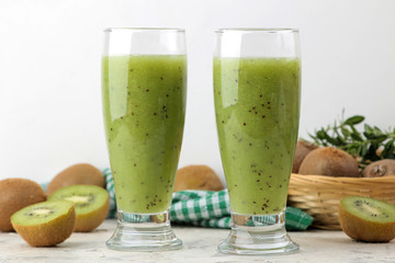Kiwi smoothies in a glass next to fresh kiwi slices on a light marble table. fruit drink.