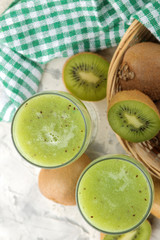 Fototapeta na wymiar Kiwi smoothies in a glass next to fresh kiwi slices on a light marble table. fruit drink. top view.