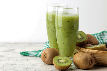 Kiwi smoothies in a glass next to fresh kiwi slices on a light marble table. fruit drink.