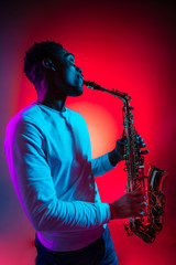 African American handsome jazz musician playing the saxophone in the studio on a neon background....
