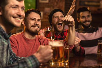 Young happy men watching football game on TV at the pub drinking beer