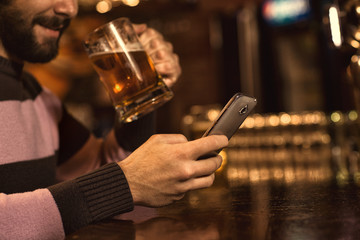 Young man using his smart phone while drinking beer