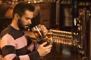 Young man using his smart phone while drinking beer